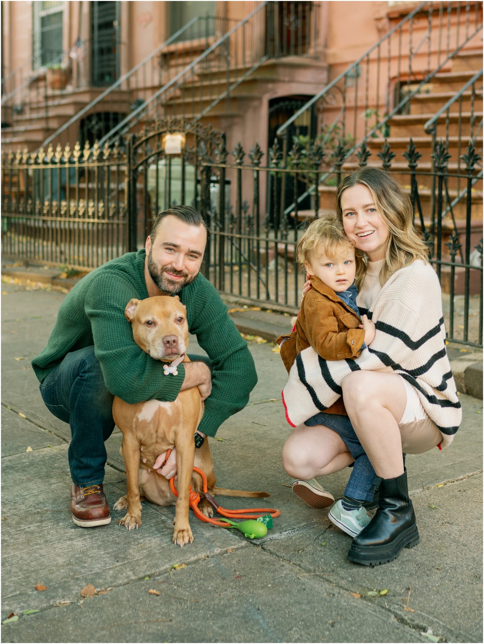 family portrait of three with dog on the sidewalk in Brooklyn, New York smiling at camera