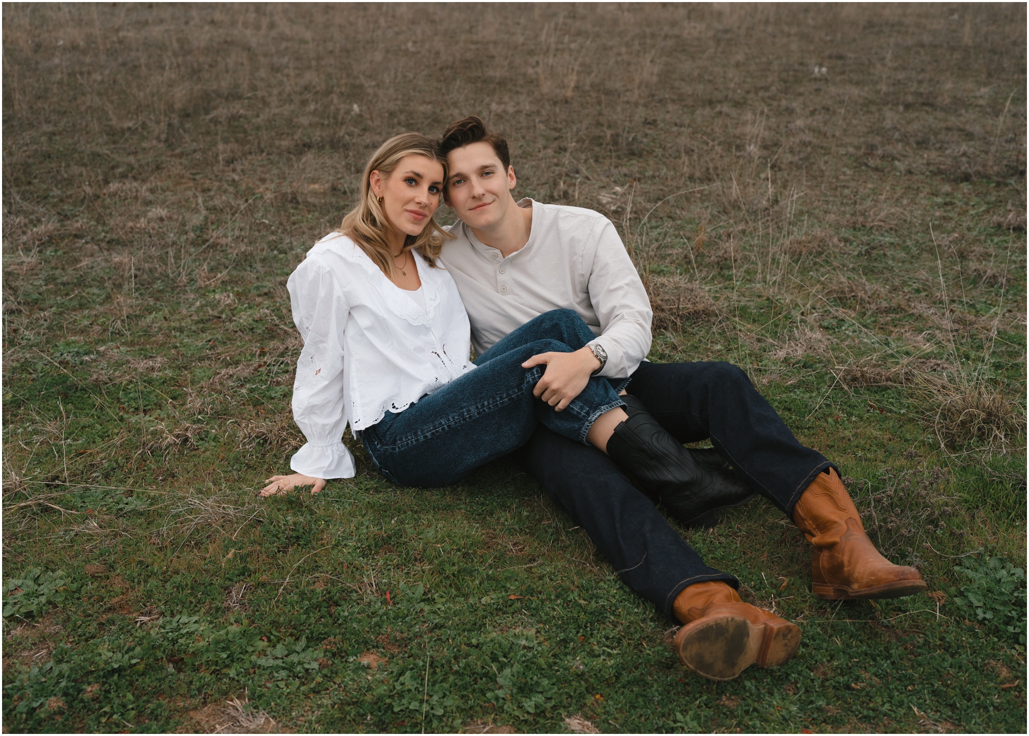 couple sitting together in tecovas boots in a field in fort worth texas engagement session