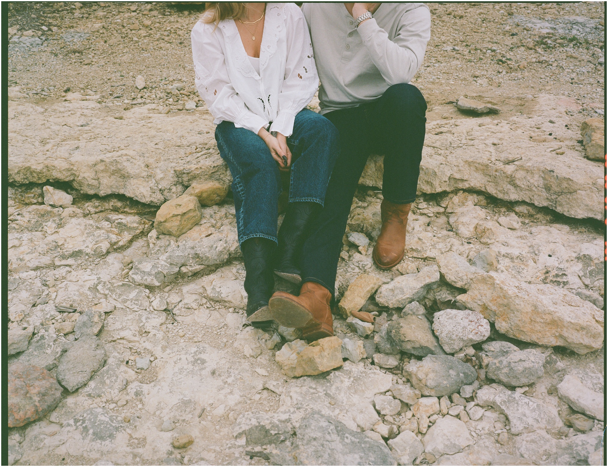 couple sitting together in tecovas boots on rocks in fort worth texas engagement session on 120mm film
